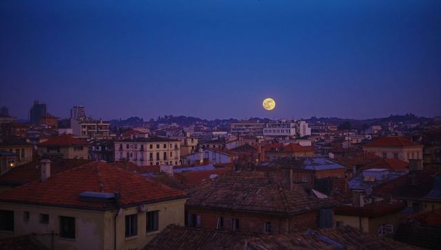 Full moon over city skyline at dusk with tiled roofs