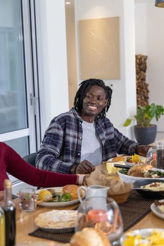 Friends sharing cozy dinner smiling african american man with dreadlocks at family table