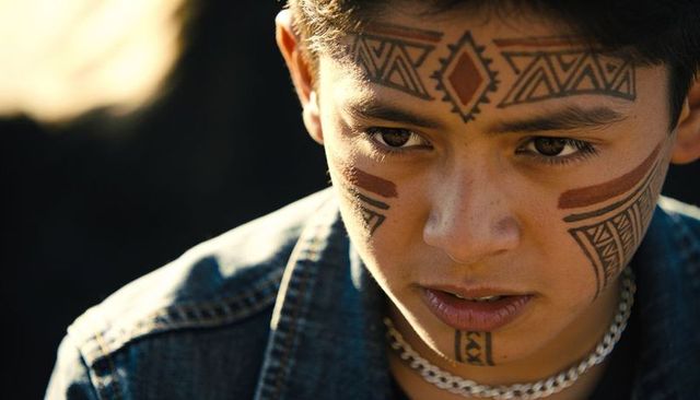 Intense teen portrait with geometric facial tattoos and silver chain in warm sunlight