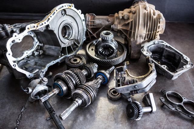 This image shows a detailed view of various car transmission parts and gears laid out on a workbench in a repair garage. Ideal for use in automotive repair manuals, engineering textbooks, industrial websites, and promotional materials for repair services. It highlights the complexity and precision of automotive engineering.