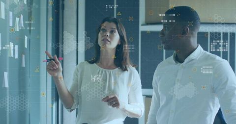 Two professionals analyzing data on glass wall in modern office