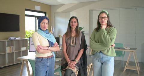 Diverse female design team reviewing laptop and blueprint while standing in modern studio