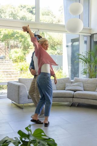 Couple dancing in sunlit modern living room woman twirling in pink shirt and jeans