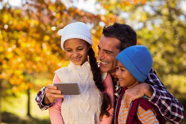Happy father with children looking at mobile phone at park during autumn