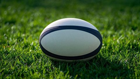 Rugby ball resting on sunlit green grass sport field