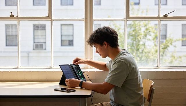 Teen charging tablet with foldable solar case at sunlit classroom desk
