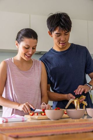 Mixed-race couple preparing fresh fruit breakfast, slicing strawberries and peeling banana
