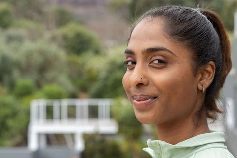 Confident indian woman smiling on balcony wearing mint-green zip-up, relaxed outdoor portrait