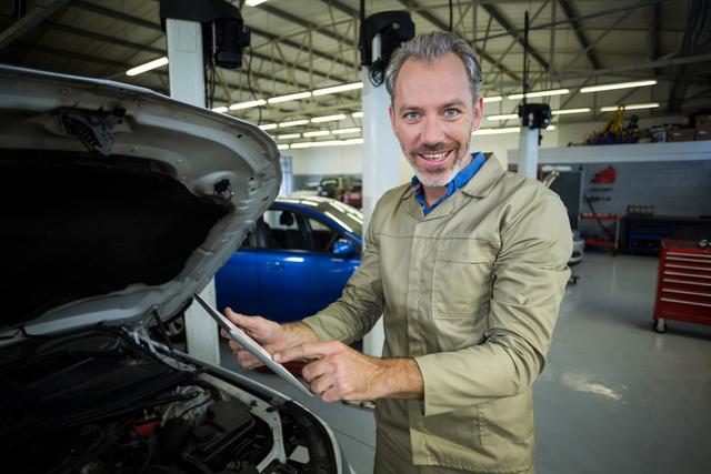 Portrait of smiling mechanic using digital tablet while servicing a car engine at repair shop
