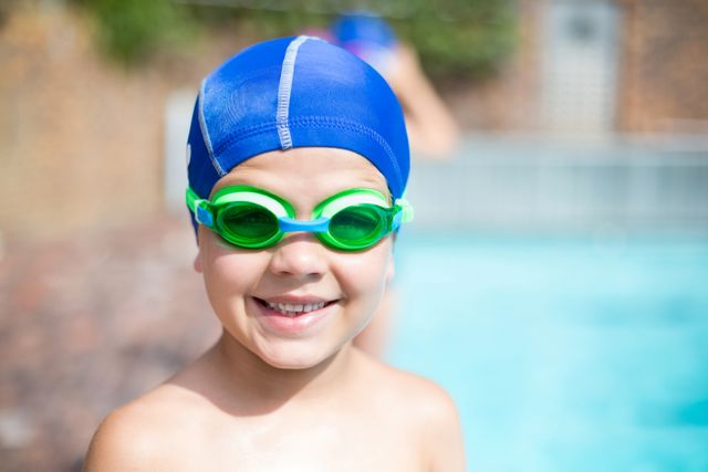 Close up portrait of little boy wearing swimming goggle and cap at poolside