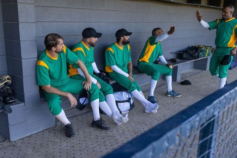 Baseball team sharing high-five in dugout wearing green and yellow uniforms