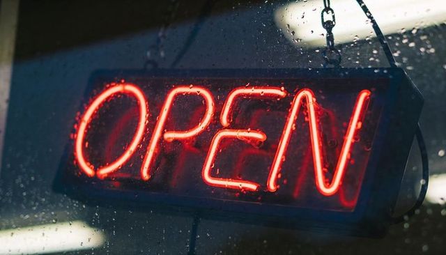 Neon open sign glowing red behind rain-speckled storefront window at night