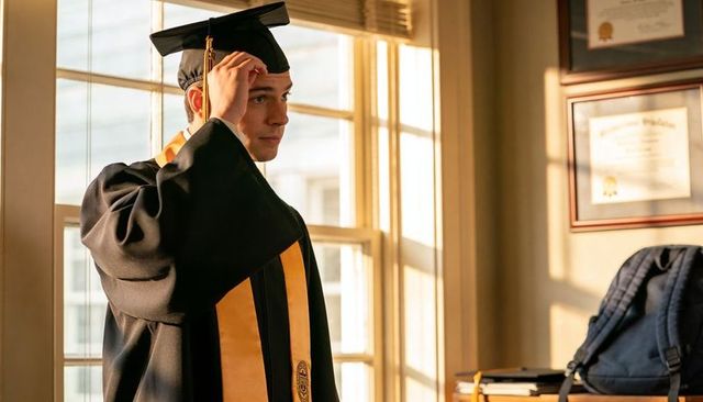 Graduating student adjusting mortarboard in warm sunlight with diploma frames and backpack