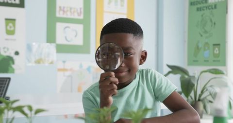 Schoolboy examining plant with magnifying glass in eco classroom exploring sustainability