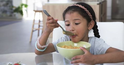 Biracial Girl Eating Cereal at Modern Breakfast Table