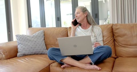 Mature Woman Laughing on Phone with Laptop at Home