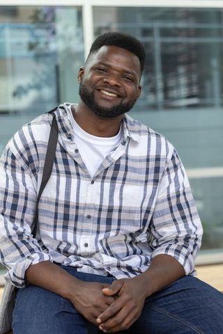 Smiling african american man in plaid shirt sitting on bench urban casual lifestyle