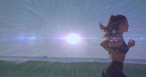 Backlit female runner sprinting along coastal path with dramatic sunburst and lens flare