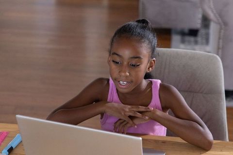 African american preteen girl doing online learning at home with laptop, school supplies