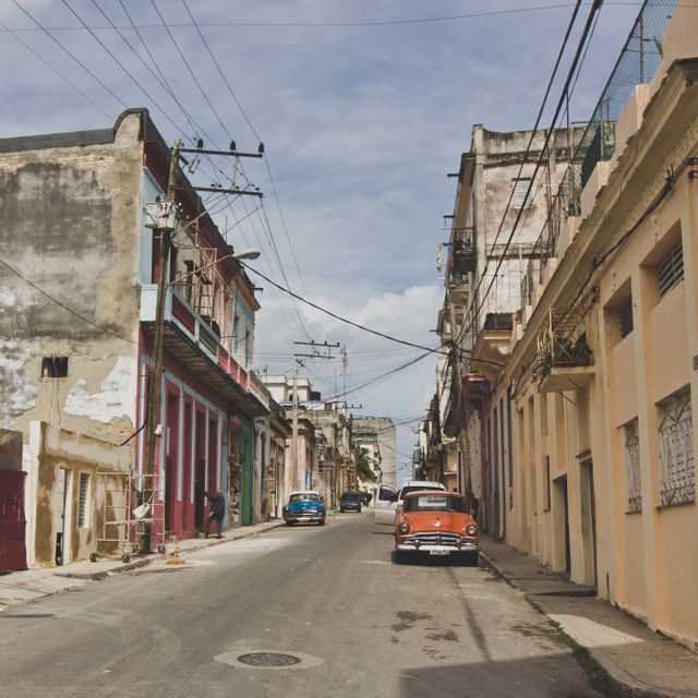 Image showcasing a typical street in Havana with colorful historical buildings and classic cars parked along the road. This scene captures the essence of Cuban culture, making it ideal for travel articles, cultural blogs, and tourism promotional materials. The vibrant facades and vintage vibe can also be used to decorate websites, brochures, and advertisements related to Latin American travel and history.