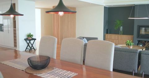 Minimalist open-plan dining featuring wooden table, gray chairs and mesh centerpiece, warm tones
