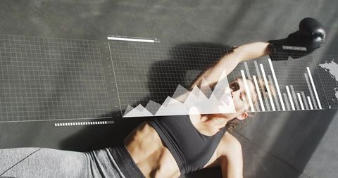 Female boxer analyzing performance data overlay while resting on gym floor in sunlight