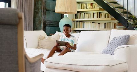 Young child using tablet in cozy living room on comfortable white sofa