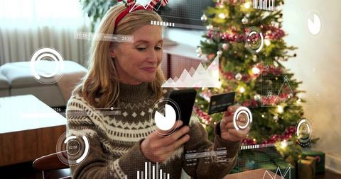 Middle-aged woman holding phone and credit card doing holiday shopping with data overlays