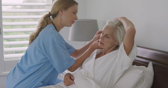 Nurse in blue scrubs assisting an elderly woman with bedside care at home. Great for use in medical, healthcare, and senior care content. Ideal for promoting home healthcare services, patient care standards, and nursing education or training.