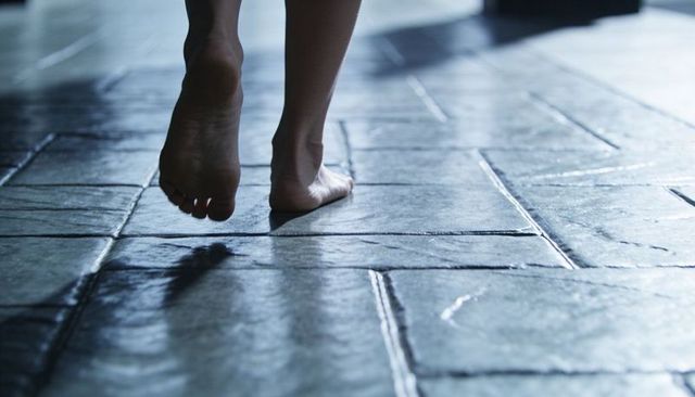 Bare feet walking on glossy tiled floor with grout reflections, shadow and textured tiles