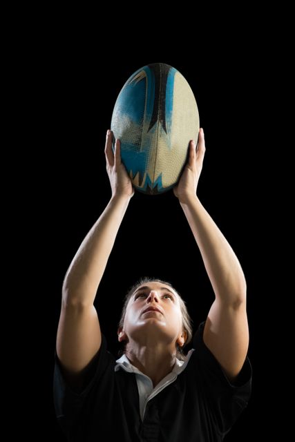 Female athlete with rugby ball against black background