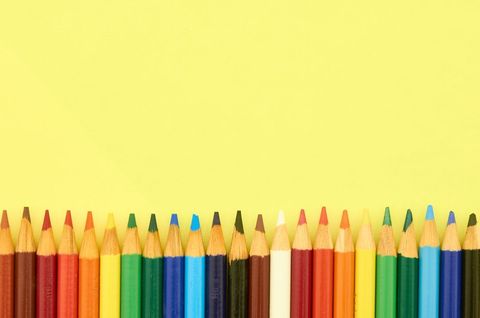 Rainbow colored pencils lining bottom edge on bright yellow background