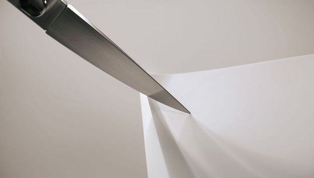 Stainless-steel knife slicing folded white paper casting sharp shadow