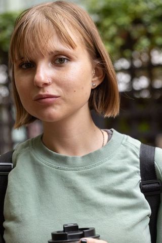 Young woman standing in urban courtyard wearing green sweatshirt holding travel mug