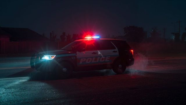 Flashing police suv lightbar lighting wet residential road at night with red blue glow