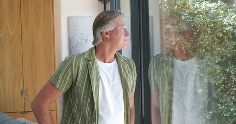 Mature man gazing through sliding glass door with reflection and garden view