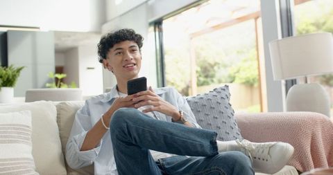 Young Man Relaxing on Sofa with Smartphone in Sunlit Living Room