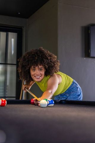 African american woman aiming cue on pool table in modern game room lounge