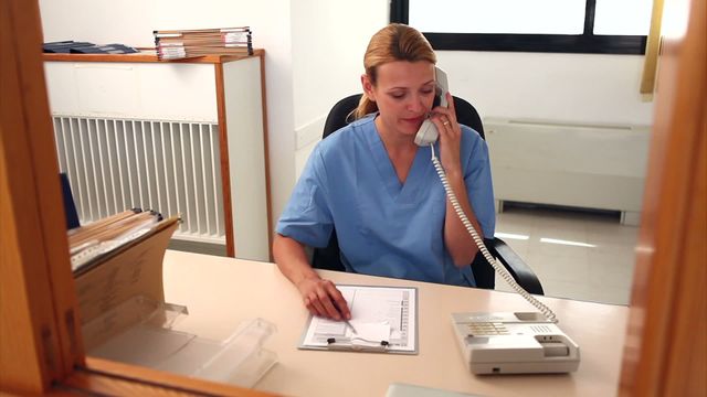 A nurse is talking on the phone while engaging with a patient, providing professional assistance at a hospital reception desk. This image conveys compassion and efficiency in healthcare service settings. Useful for illustrating medical, healthcare, hospital themes in brochures, websites, or training materials related to patient care and hospital operations.