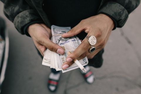 Person holding cigarette and counting dollar bills in hand