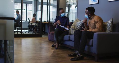 Colleagues discussing in office while masked during pandemic
