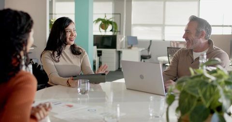 Diverse team collaborating around conference table with tablet and laptop in bright office