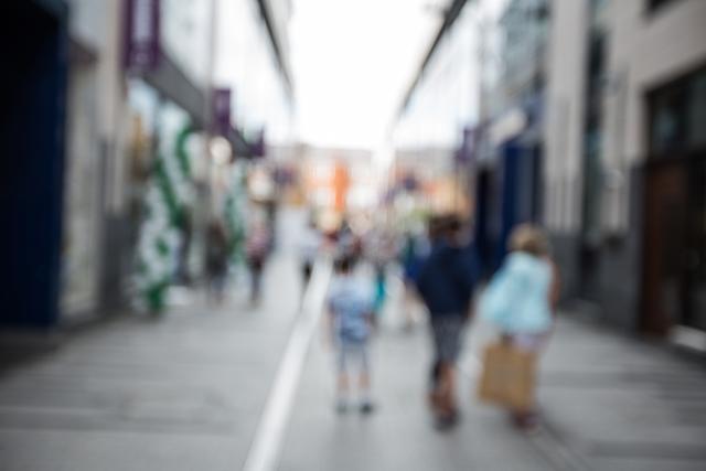 Image showing blurred pedestrians walking on a city street during a sunny day. Perfect for use in concepts of urban lifestyle, city life, daily commutes, or illustrating movement and activities in modern urban environments.