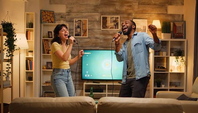 Couple singing karaoke at home using tv and wired microphones in cozy living room evening