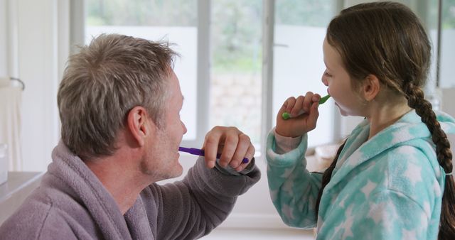 Father and daughter brushing teeth together in bathroom wearing robes. Ideal for illustrating family bonding, morning routines, hygiene habits, and parental care. Suitable for health and wellness promotions, personal care products, or family lifestyle articles.