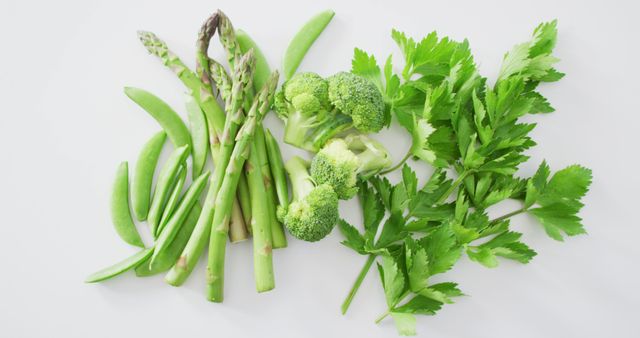 Assorted fresh green vegetables including asparagus, snap peas, broccoli, and celery leaves arranged on a white background. Perfect for use in grocery advertisement, healthy food blog posts, vegan recipe illustrations, or diet and nutrition promotions.
