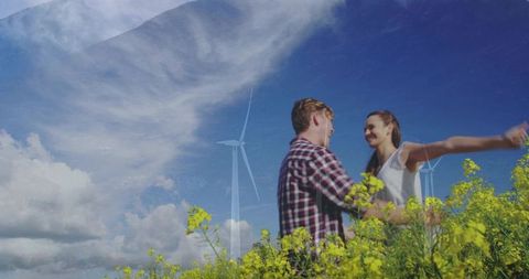 Young couple embracing in sunlit canola field with wind turbines and blue sky