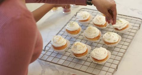 Mother and child decorating frosted cupcakes with gold sprinkles on cooling rack