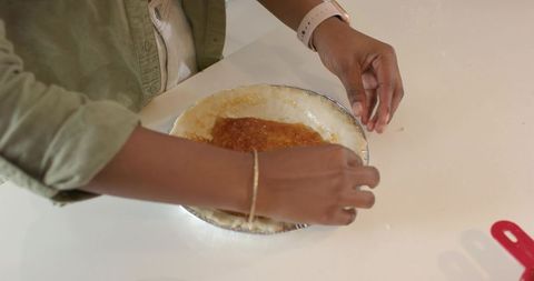 African american woman pressing pie crust with jam filling into tin on kitchen counter
