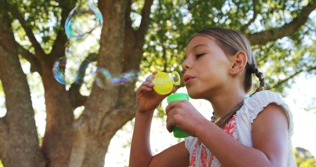 A young girl is blowing bubbles in a park, with copy space. Her focused expression and the outdoor setting create a playful and carefree atmosphere.